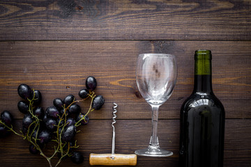 Composition with wine. Red wine bottle, bunch of grapes, corkscrew, wine glass on dark wooden background top view copy space