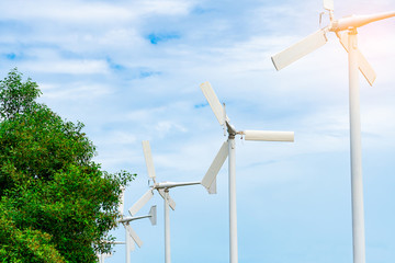 Horizontal axis wind turbine with blue sky and white clouds near green tree. Wind energy in eco...