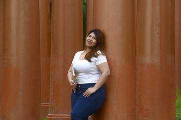 Asian pretty smiley face fat woman pose standing and hold a booklet on group of pole in the park.