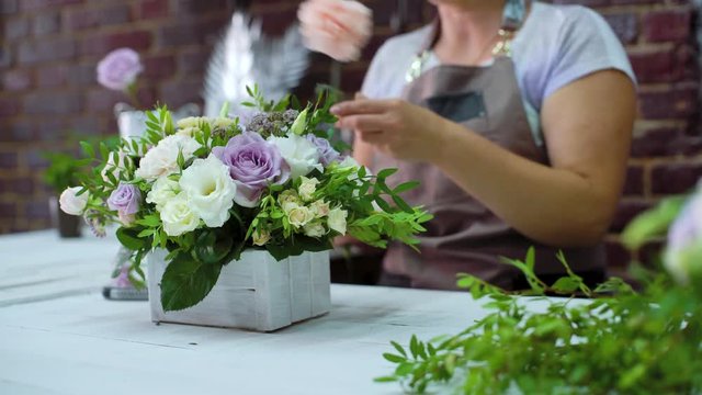 professional florist arranging beatiful flower composition in wooden box in floral design studio. Caucasian female master in apron creating floral design. Floristry, handmade, small business concept