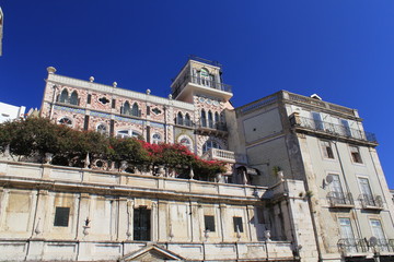 An old multi-storey building with mosaic, balconies and pots with flowers against the blue sky