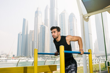 Portrait of a handsome man doing push ups exercise on a bars outdoors