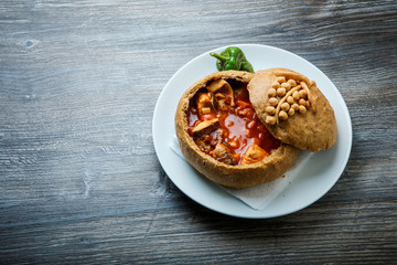 fish soup in original homemade brown bread bowl on white plate with green pepper