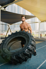 Fototapeta na wymiar Young arab sports man exercising with truck tyre outdoors in Dubai during summer time.