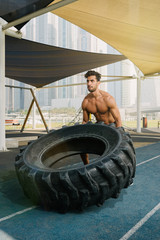 Obraz na płótnie Canvas Young arab sports man exercising with truck tyre outdoors in Dubai during summer time.