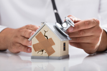 Doctor examining broken house with stethoscope