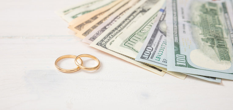 Golden wedding rings and banknotes dollars, on a white wooden background, banner. - Powered by Adobe