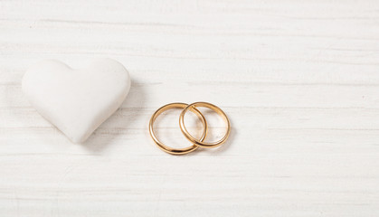 Close up view of golden wedding rings and a white heart, isolated, copy space, on a white wooden...