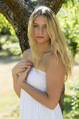 Young model with long blonde hair posing in park in sunshine