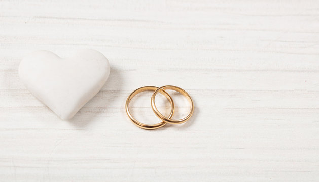Close up view of golden wedding rings and a white heart, isolated, copy space, on a white wooden background.