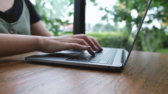 Closeup image of a business woman's hands working and typing on laptop keyboard on wooden table with green nature background