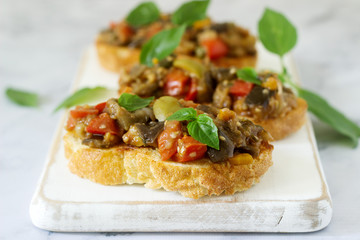 Bruschetta with caponata or ratatouille from various vegetables on a light background.