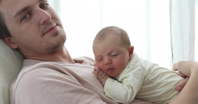 Side view of casual man sitting with charming little newborn baby on hands kissing in head