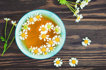 Obraz na płótnie Canvas Top view of organic chamomile tea with fresh flowers on a wooden table. The concept of healthy eating and alternative medicine.