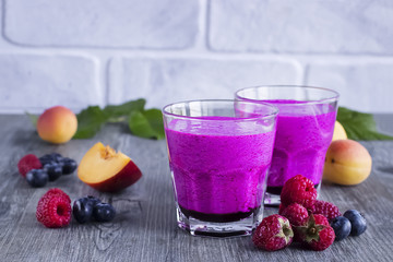 Homemade smoothies of fresh berries and fruits in glasses on gray wooden table.