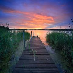Dramatic Sunset over Lake with wooden Pier and Reeds