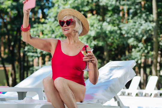 Making selfie. Modern beaming retired woman wearing stylish straw hat making selfie in swimming suit - Powered by Adobe