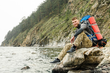 Young guy tourist with backpack on lake and mountains background
