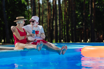 Funny pensioners. Couple of happy funny pensioners feeling unbelievable while drinking cocktails near pool