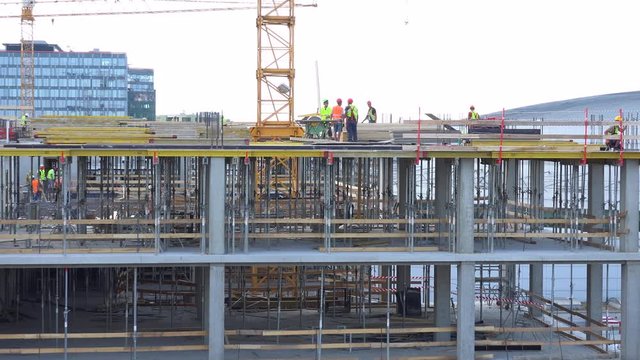 A group of workmen work on the top of a building under construction - the bright sky in the background