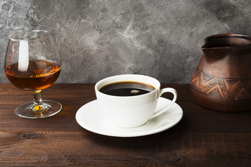 Coffee in white cup with cognac and clay cezve on wooden background