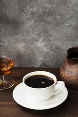Coffee in white cup with cognac and clay cezve on wooden background. Copy space. Food background