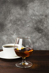 Glass of cognac and coffee in white bowl on wooden background