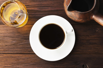 Coffee in white cup with cognac and clay cezve on wooden background. Top view. Food background
