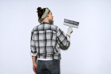 young slender girl in a plaid shirt leveling the walls with a spatula
