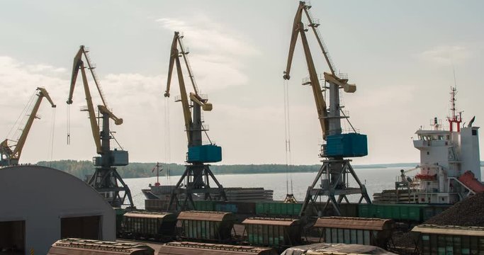 Port Cranes During Operation. The port marine crane unloads coal from railway cars to a dry cargo ship in the background of the gulf