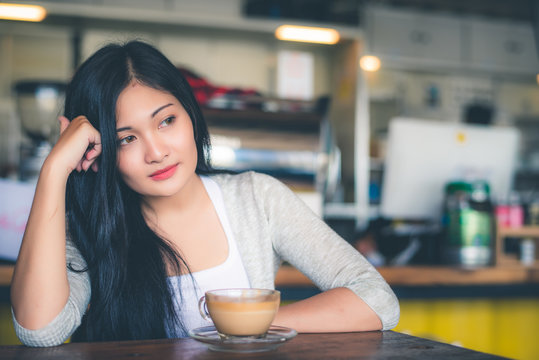 Beautiful attractive young Asian woman holding a cup of coffee or coffe in hand at cafe in the morning, vintage color tone. 