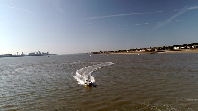 Drone flies back from approaching speedboat on the River Mersey. Liverpool and New Brighton Beach in the background 