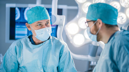 Portrait Shot of a Diverse Team of Professional Surgeon and Assistants Performing Invasive Surgery on a Patient in the Hospital Operating Room. Surgeons Have Active Discussion Trying to Save Life