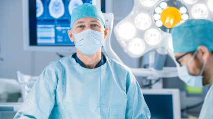Portrait Shot in the Operating Room, of a Surgeon Looking into Camera During Operation. Professional Medical Doctors Performing Surgery.