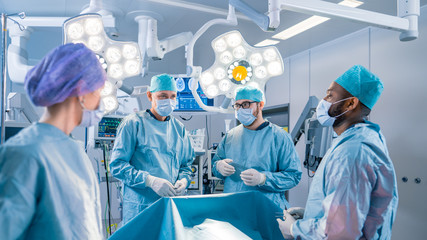 Diverse Team of Professional surgeon,  Assistants and Nurses Performing Invasive Surgery on a Patient in the Hospital Operating Room. Surgeons Have Active Discussion About to Saving Life of a Patient.