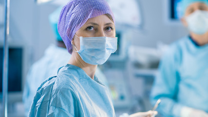 Portrait Shot of a Nurse Looking into Camera During Operation in the Operating Room. Professional Medical Doctors Performing Surgery.