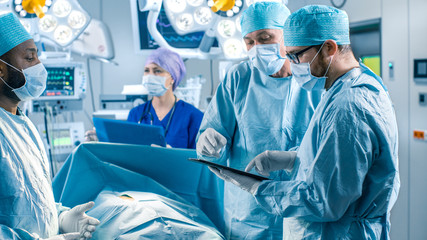 Professional Surgeons and Assistants Talk and Use Digital Tablet Computer During Surgery. They Work...