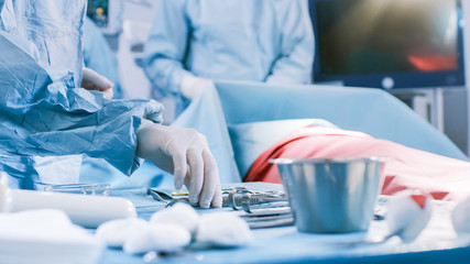 Close-up Shot in the Operating Room of Surgical Table with Instruments, Assistant Hands out Instruments to Surgeons During Operation. Surgery in Progress. Medical Doctors Performing Surgery.