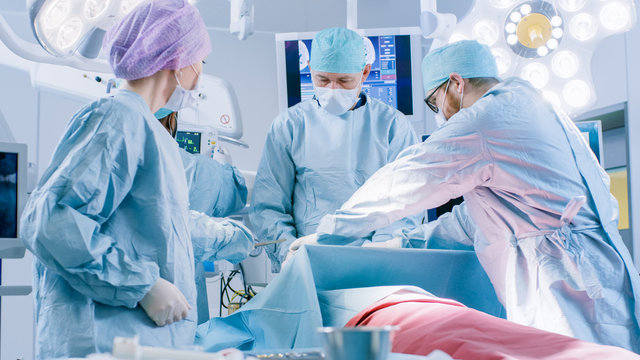 Diverse Team of Professional Surgeons Performing Invasive Surgery on a Patient in the Hospital Operating Room. Surgeonst Use  and other Instruments, Anesthesiologist Monitors Vitals.