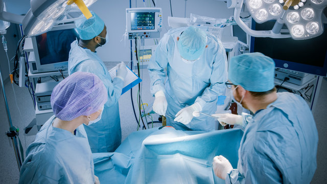 Diverse Team of Professional surgeon,  Assistants and Nurses Performing Invasive Surgery on a Patient in the Hospital Operating Room. Surgeons Talk and Use Instruments. Real Modern Hospital