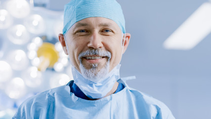 Portrait of the Professional Surgeon Takes off Surgical Mask after Successful Operation Simling Into Camera. In the Background Modern Hospital Operating Room. - Powered by Adobe