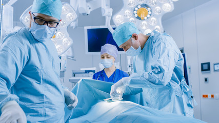 In the Hospital Operating Room Diverse Team of Professional Surgeons and Nurses Suture Wound after Successful Surgery. Surgeon Take Surgical Instrument.