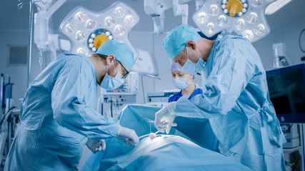 In the Hospital Operating Room Diverse Team of Professional Surgeons and Nurses Suture Wound after...