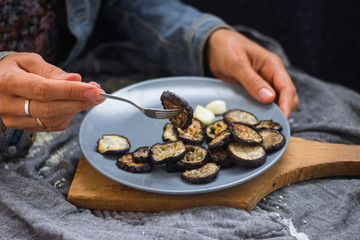 Woman hands sticks on fork roasted eggplants slices fro stylish grey plate. Sprinkled with herbs, black pepper and garlic powder. Perfect vegan dish. No refined oil. Vegetarian lunch. Small portion
