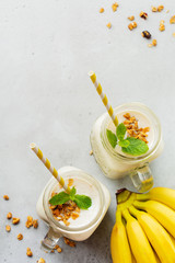 Banana smoothie with granola, dried fruits and mint on gray concrete background. Top view.