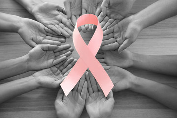 Female hands holding pink ribbon on wooden background, top view. Breast cancer awareness concept