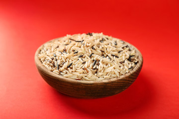 Bowl with raw rice on color background