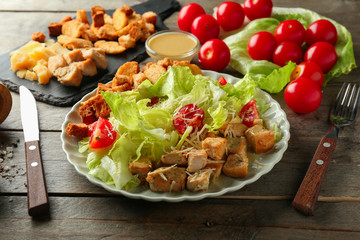 Plate with tasty Caesar salad on wooden table