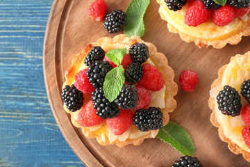 Tasty tartlets with berries on wooden board, closeup