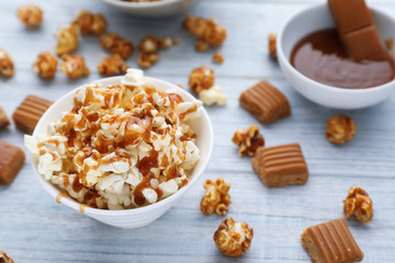 Bowl full of delicious popcorn with caramel on wooden background